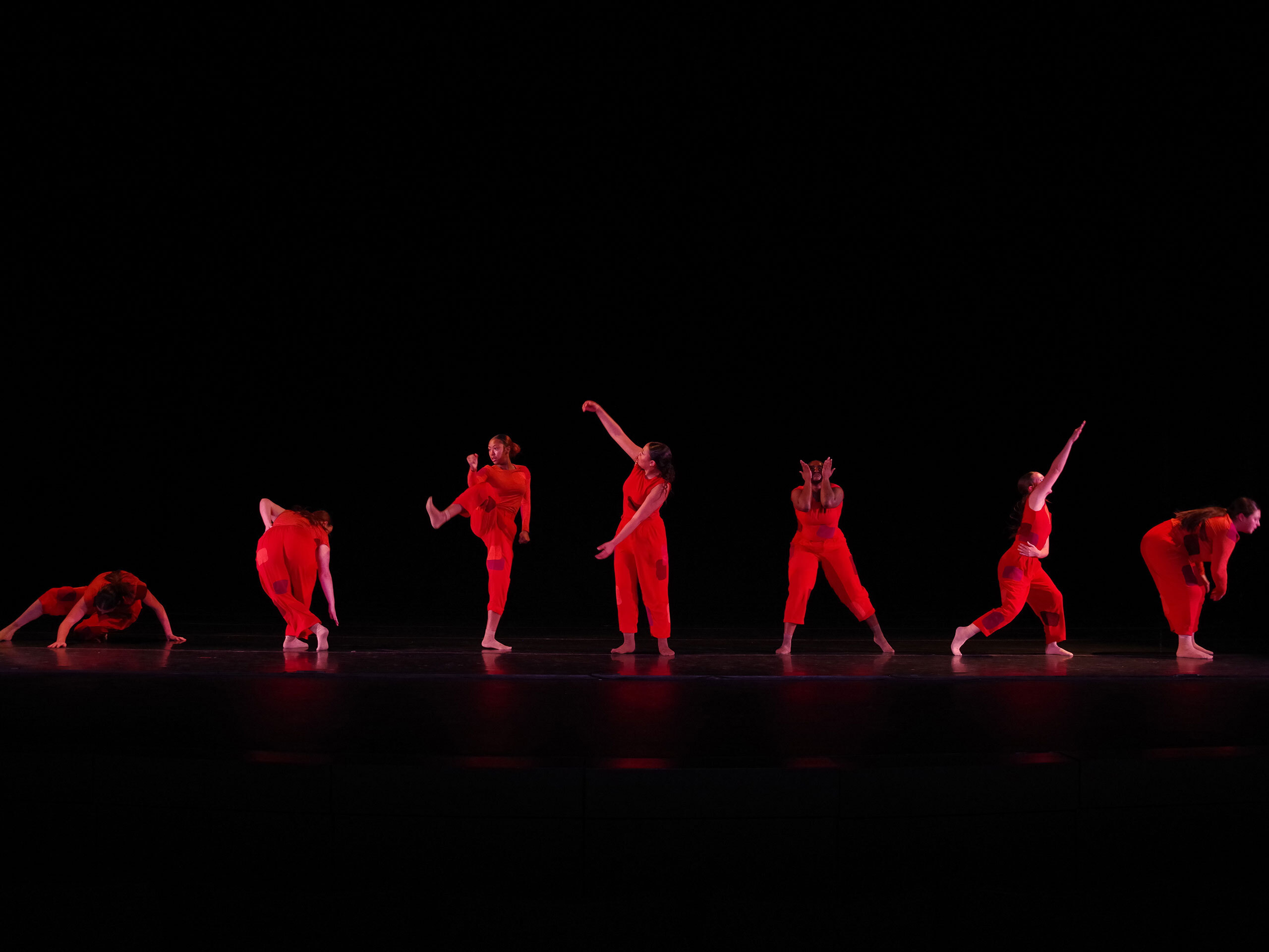 Five female students in colorful outfits strike various dance poses on top floor of a campus parking garage.
