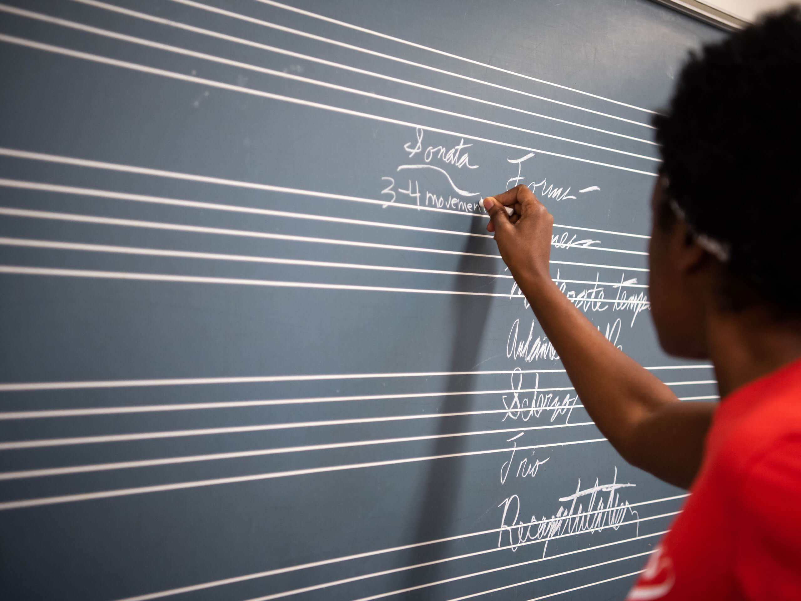 Person writing on a chalkboard designed like a musical staff.