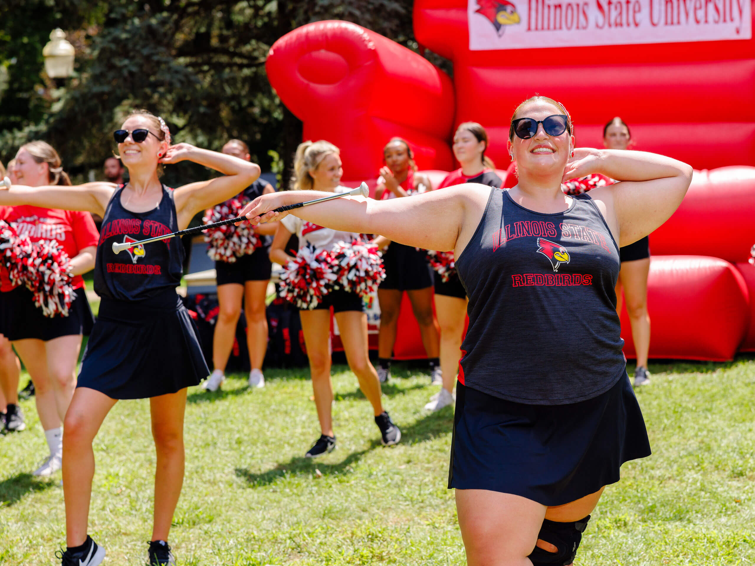 Cheerleaders performing with batons in front of a red inflatable backdrop.