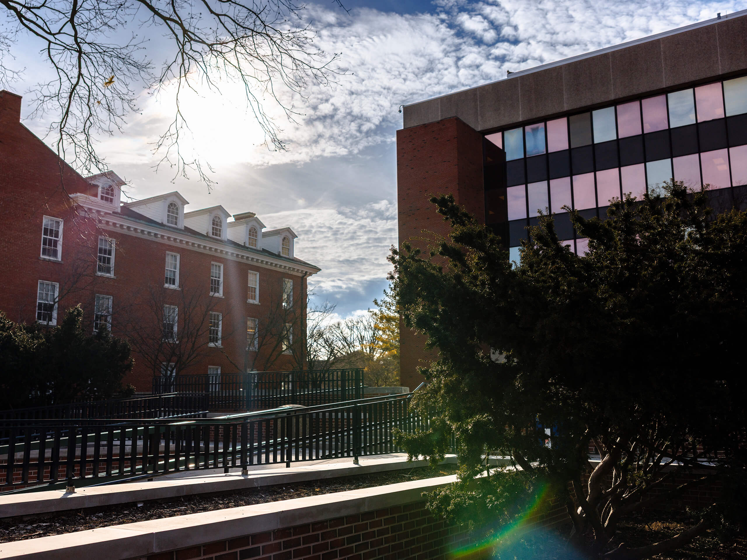 Two buildings on a campus, one traditional red-brick and one modern with glass panels, under a partly cloudy sky.