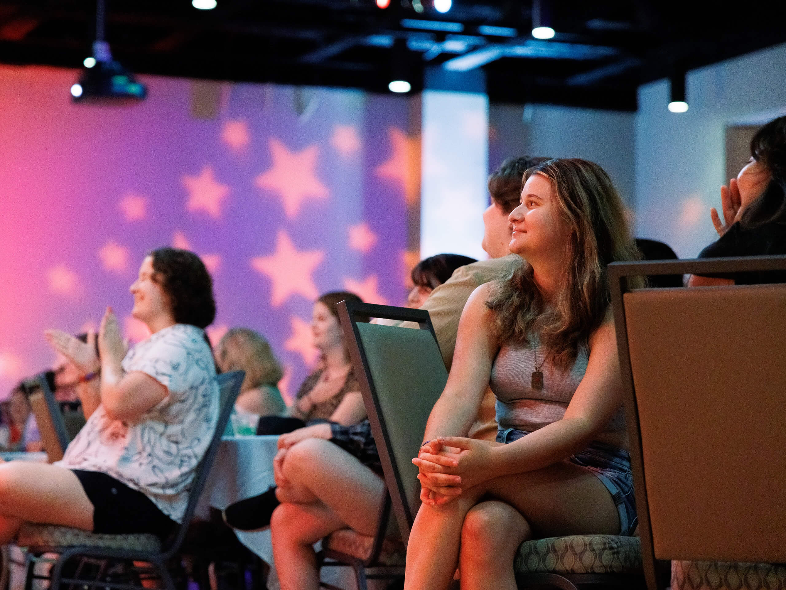 People seated in a dim room with star-shaped lights projected on the wall.