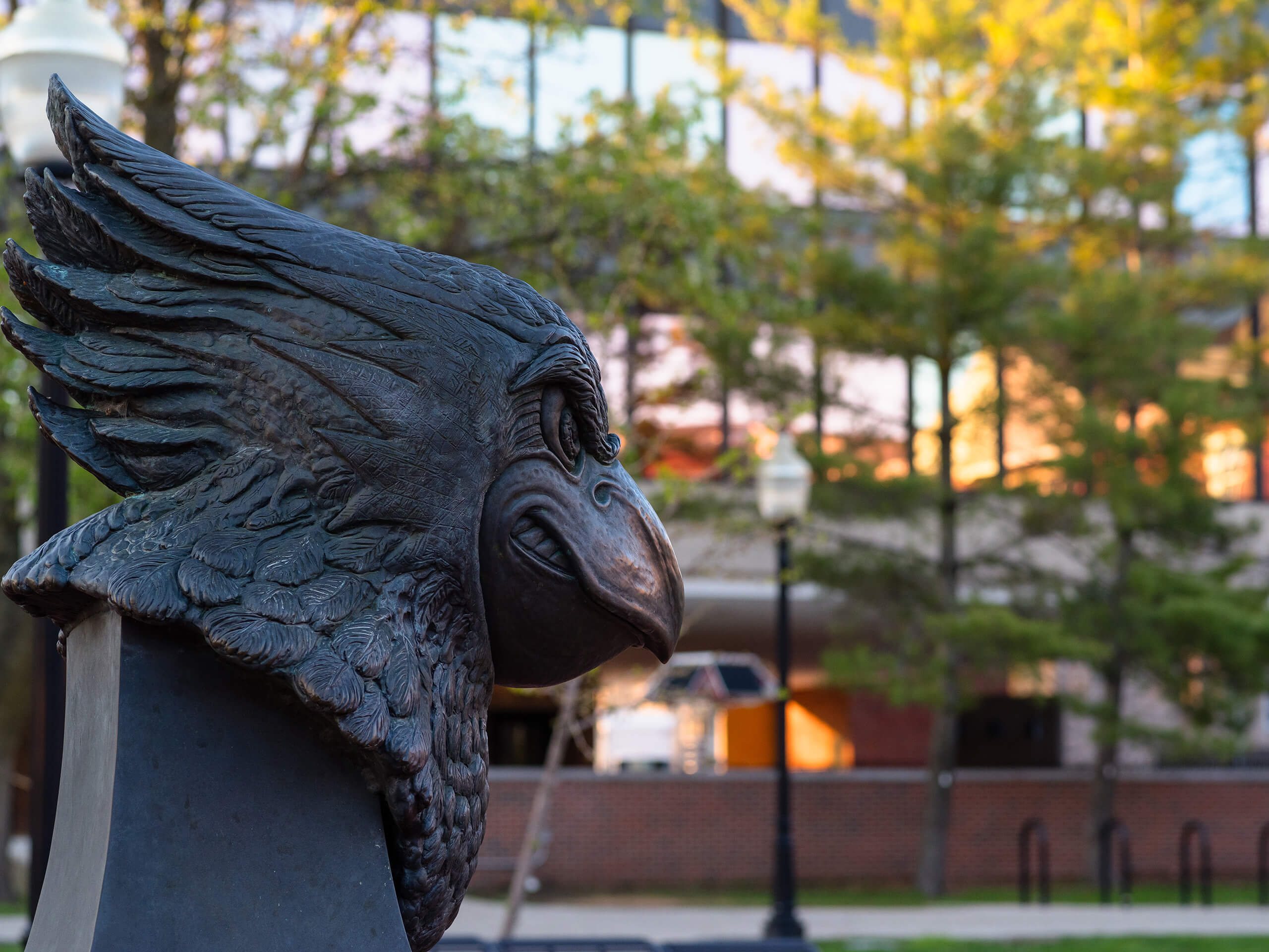 A bronze bust of Reggie Redbird with detailed feathers against a building and tree backdrop.